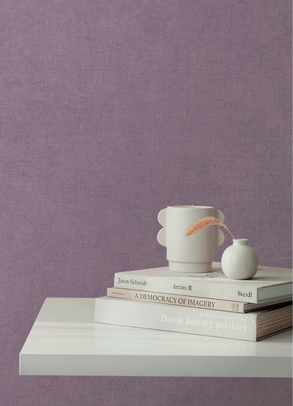 A styled interior scene with a lavender-purple textured wall, a white floating shelf, stacked books, a white ceramic mug, a small white vase, and a dried orange flower.